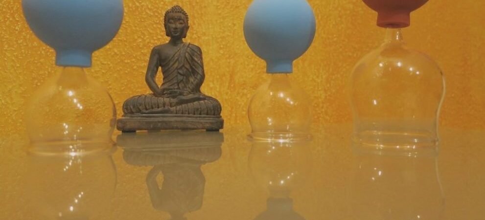 Gesundheitspraxis Oberfranken: Die Buddha Skulptur sitzt zwischen den Schröpfgläsern