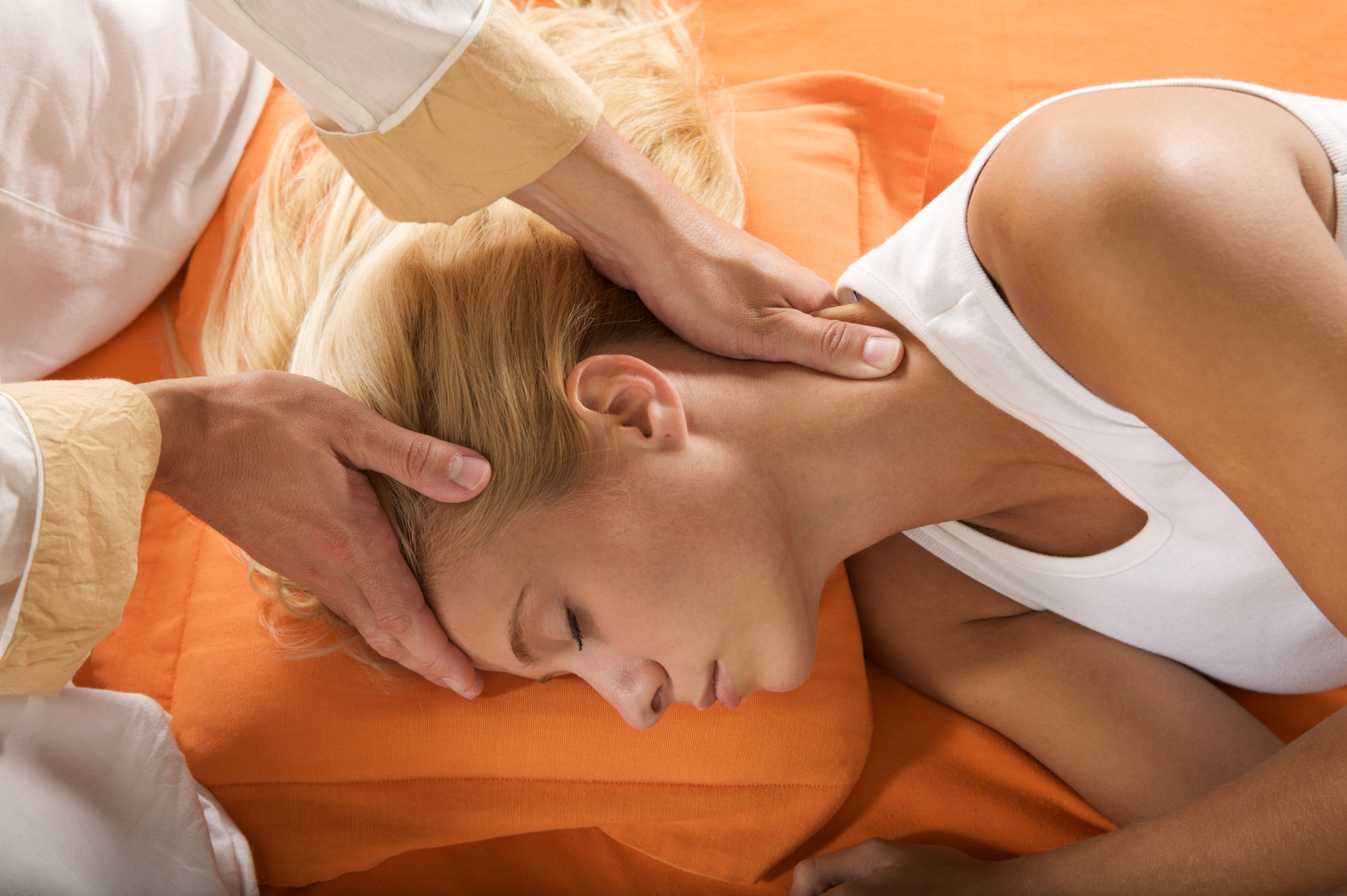 Junge Frau mit blonden hochgesteckten Haaren liegt mit ihrer rechten Seite auf dem Boden und bekommt eine achtsame KopfM massage von einem Mann mit sanften Händen